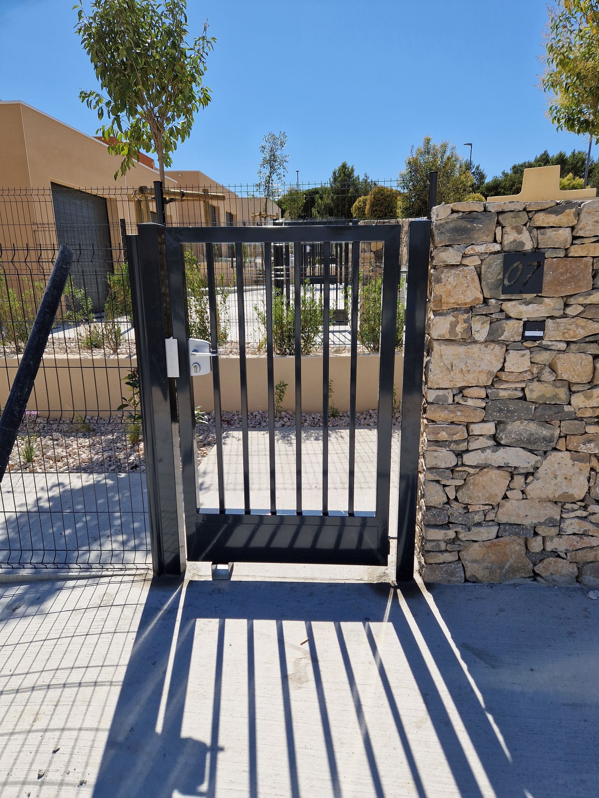 Vue arrière d'un portail électrique avec mur de pierre et grillage