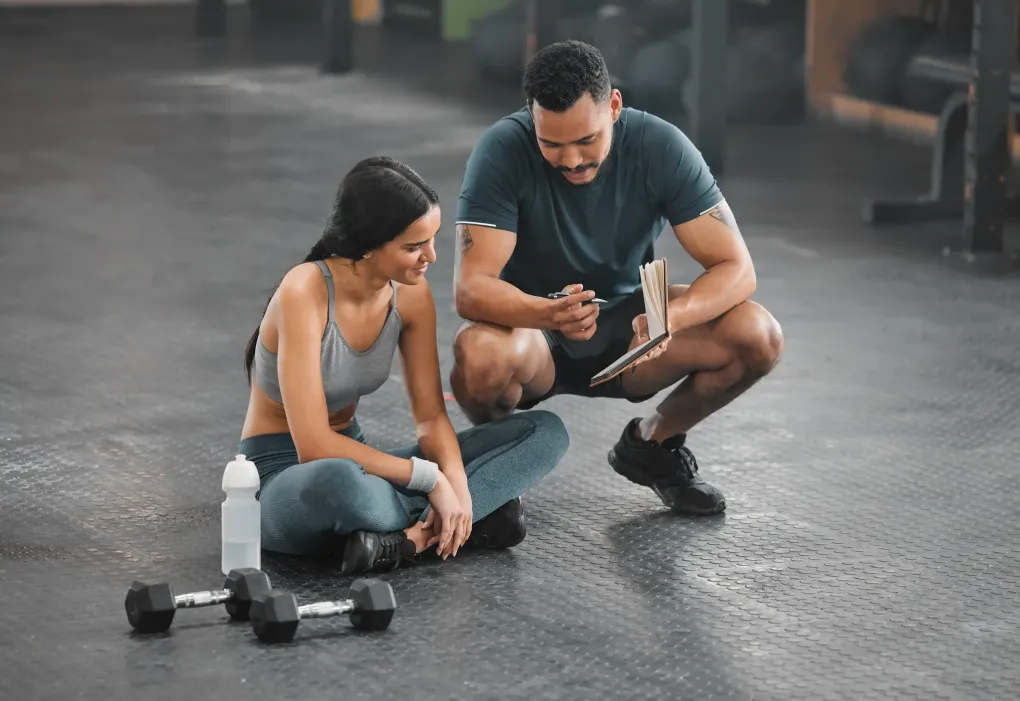 Un hombre y una mujer están sentados en el suelo en un gimnasio.