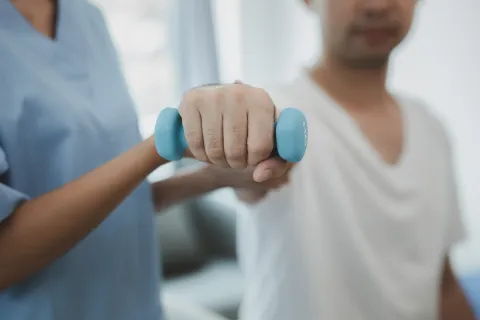 Una enfermera está ayudando a un paciente a levantar una mancuerna azul.