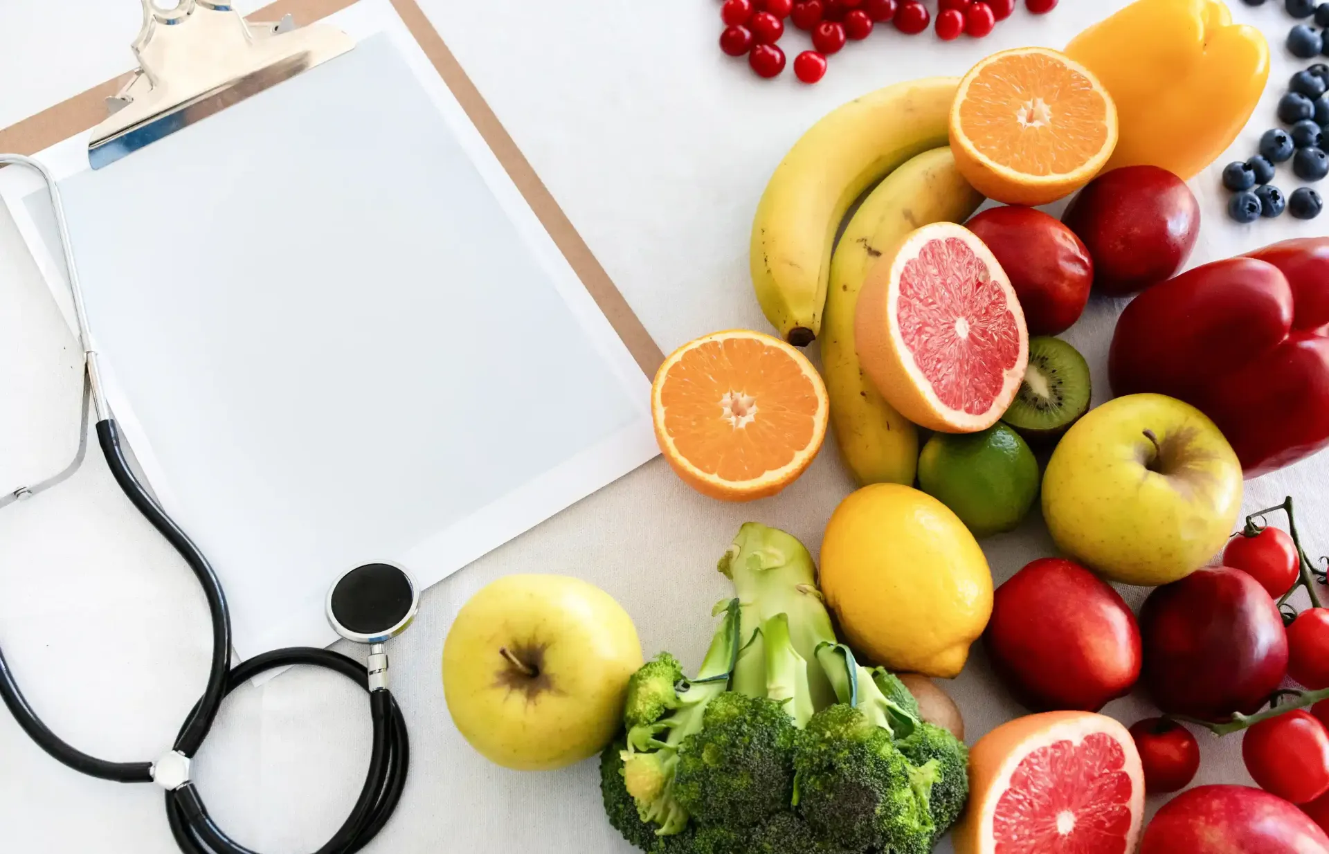 Un estetoscopio, un portapapeles, frutas y verduras sobre una mesa.