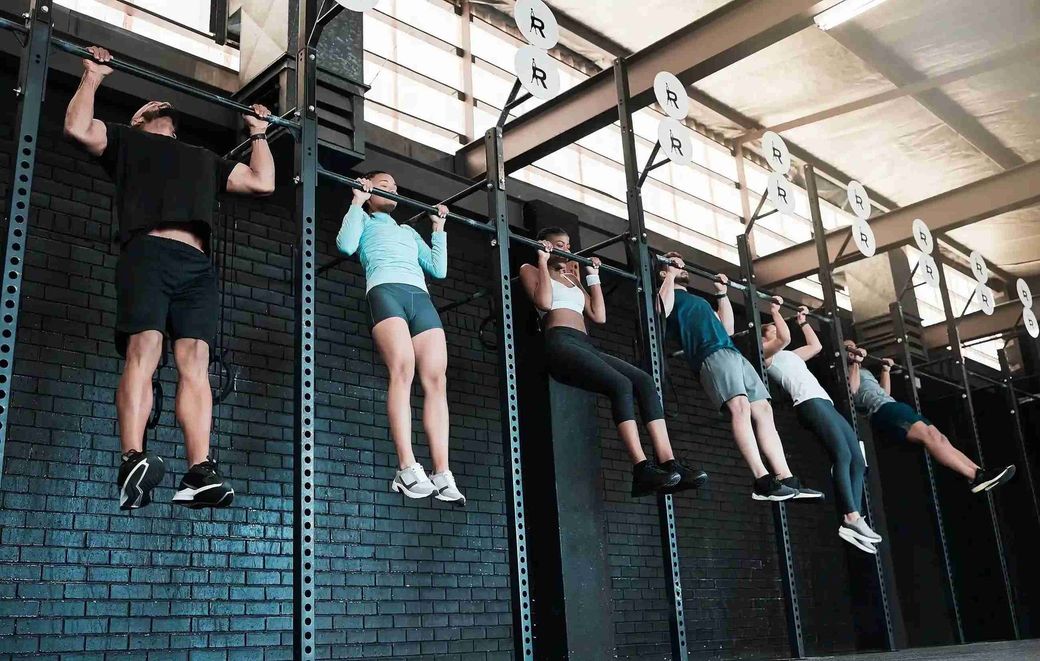 Un grupo de personas está haciendo dominadas en una pared de un gimnasio.