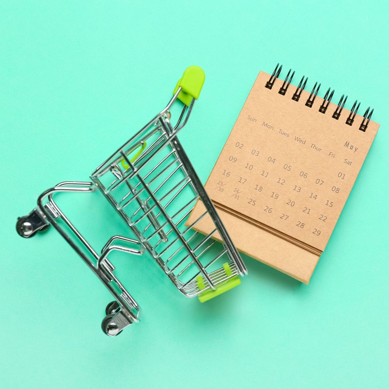 Un carrito de compras junto a un calendario sobre un fondo verde