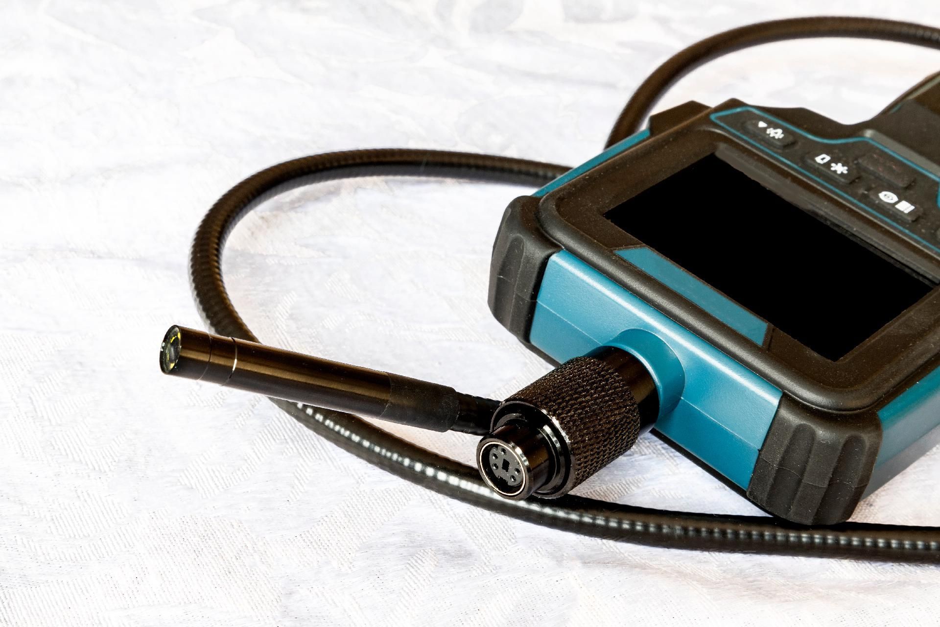 Inspektionskamera Blaue, handgeführte digitale Inspektionskamera mit angeschlossenem Kabel und Sonde auf einer weißen Oberfläche