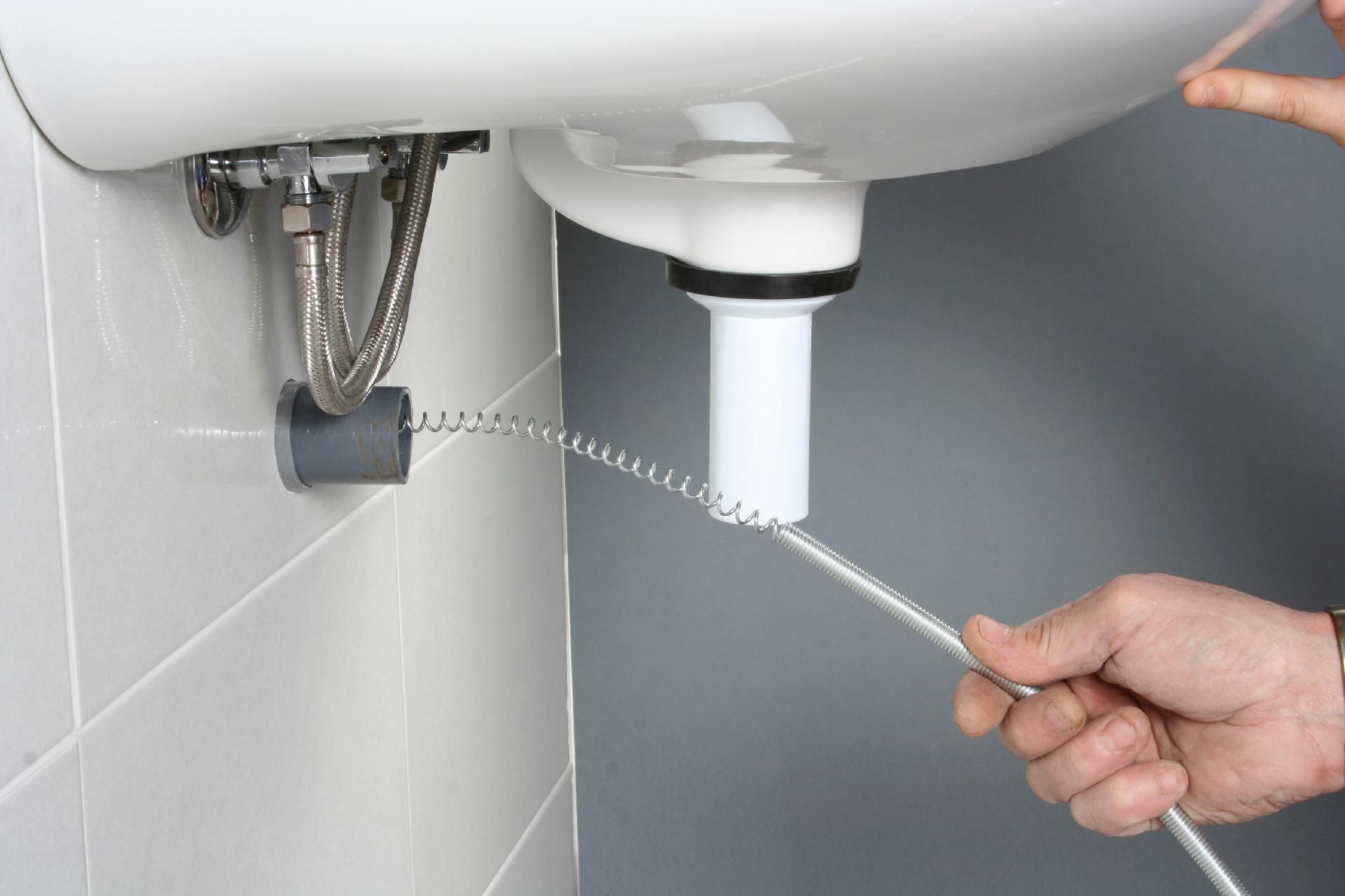 Abflussspirale Mit einer Abflussspirale wird der Abfluss eines Waschbeckens unter einem weißen Becken im Badezimmer gereinigt.