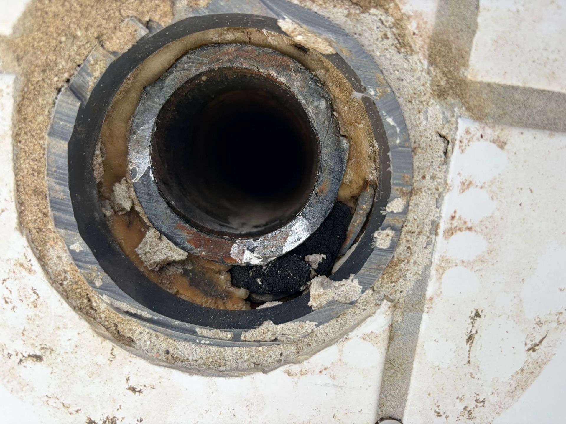 Nahaufnahme einer verrosteten Metallrohröffnung in einer abgenutzten weißen Oberfläche