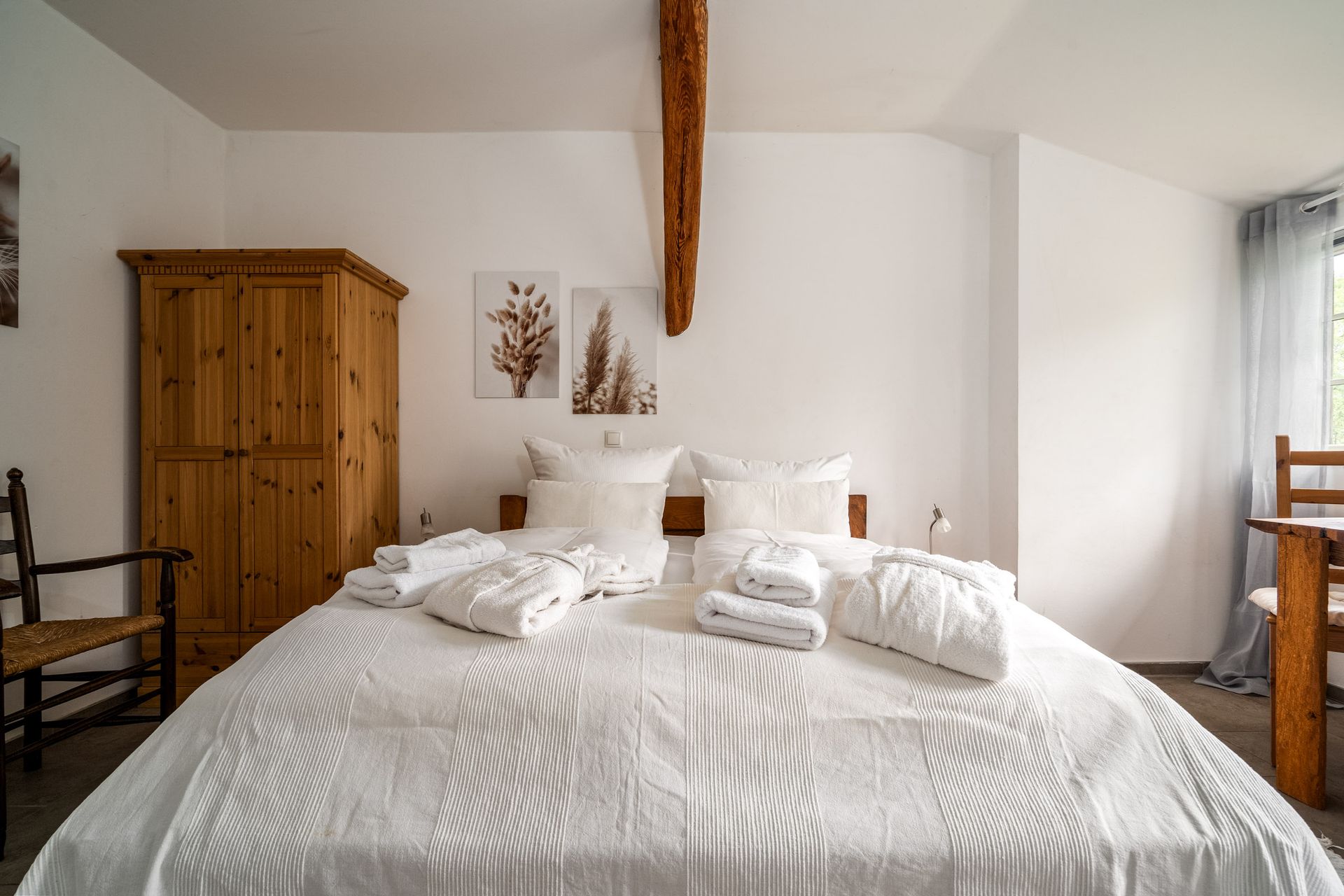 Helles Schlafzimmer mit weißem Bett, Holzschrank und sichtbaren Deckenbalken
