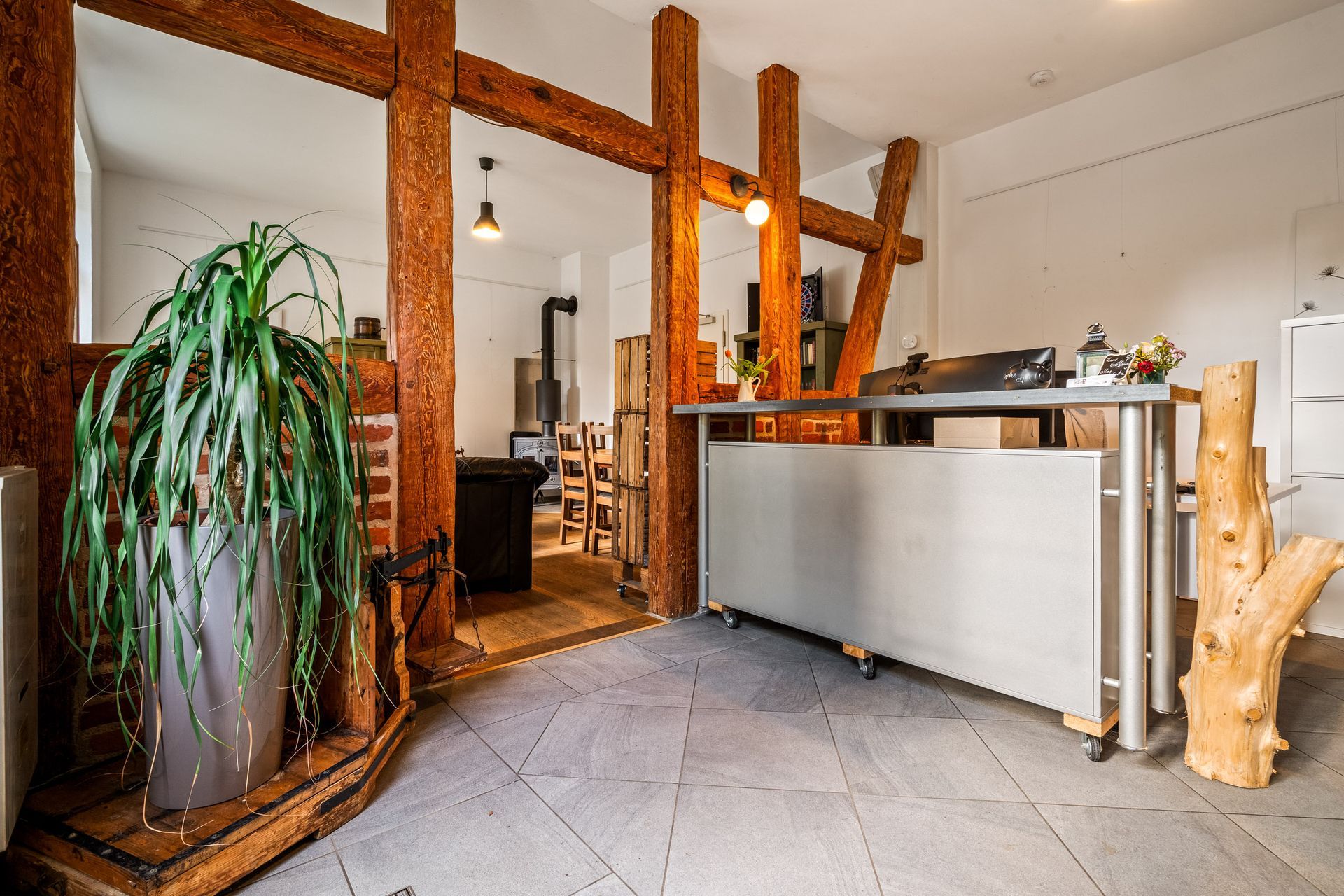 Moderne Lobby mit Holzbalken, großer Topfpflanze und grauem Empfangstresen in rustikalem Interieur.