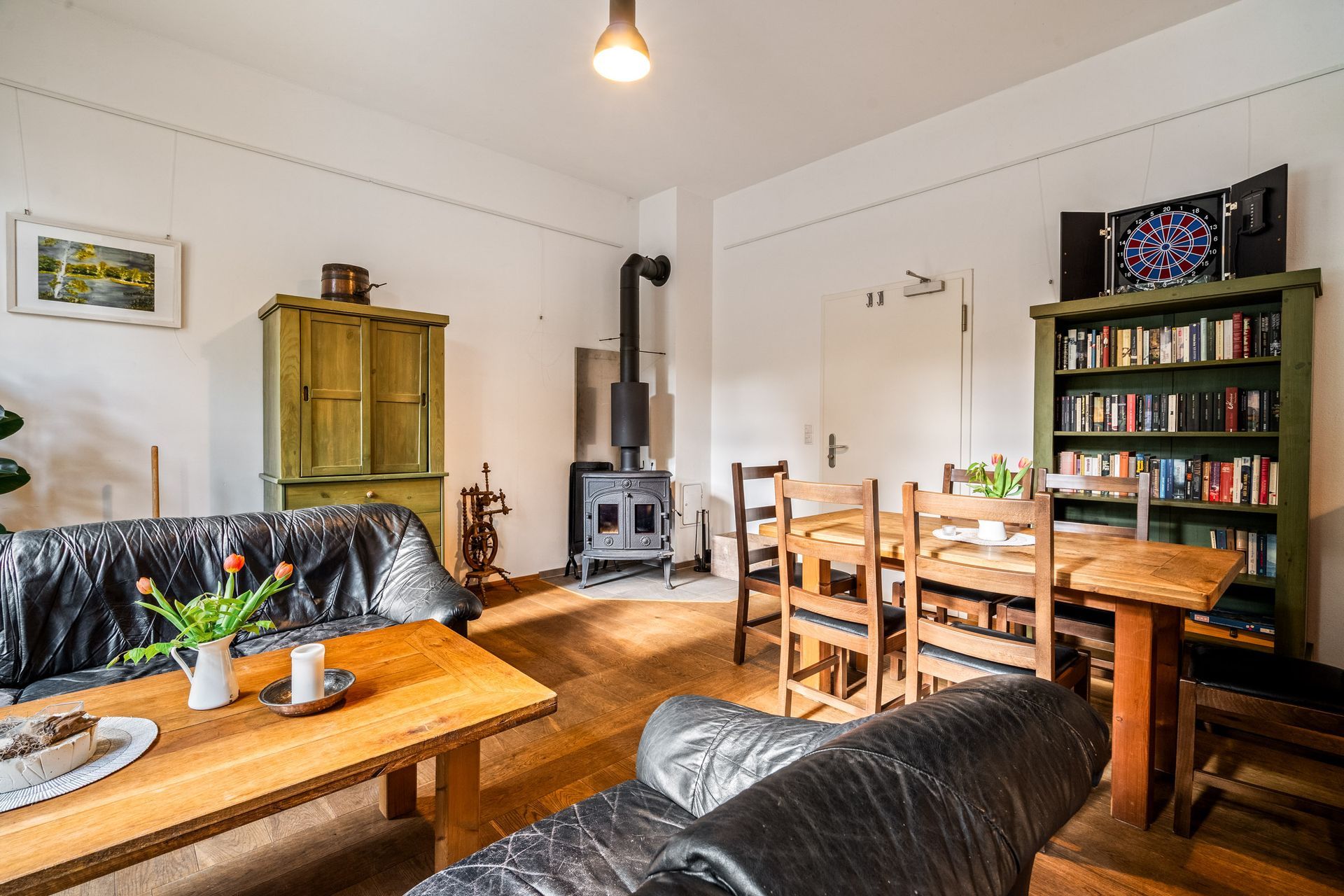 Gemütliches Wohn-Esszimmer mit Holzofen, schwarzen Ledersofas, Holztisch und Bücherregal