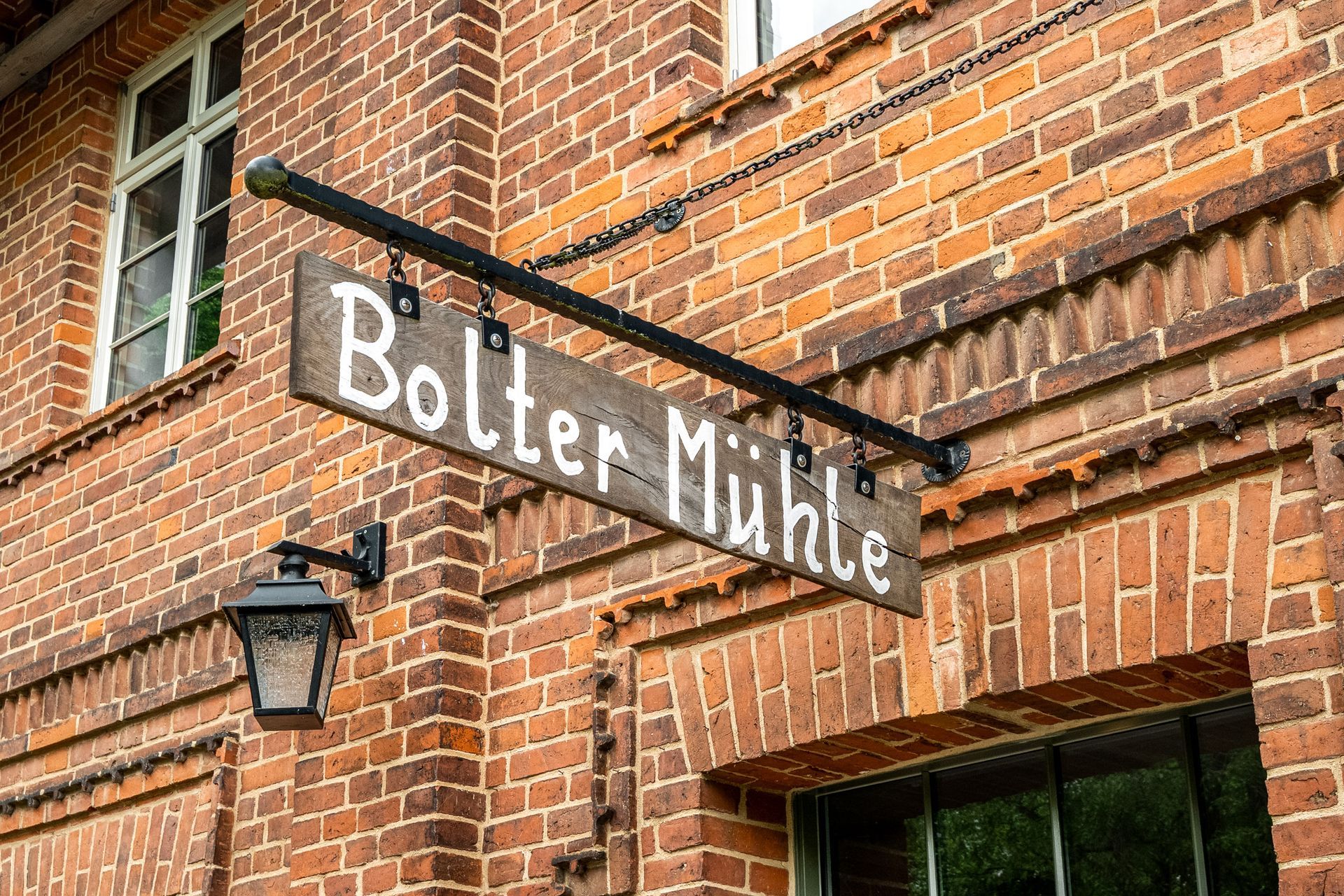Schwarzes Hängeschild mit der Aufschrift „Bolter Mühle“ an der Außenfassade eines Backsteingebäudes