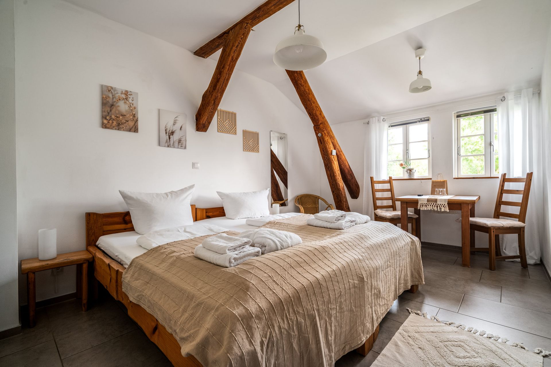 Helles Schlafzimmer mit Doppelbett, Holzbalken und einem kleinen Esstisch am Fenster.