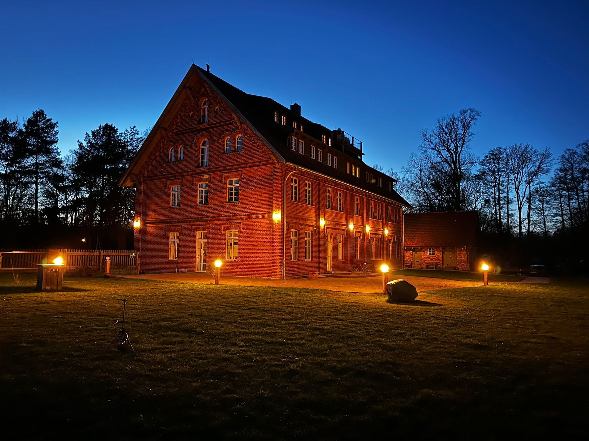 Beleuchtetes rotes Backsteinhaus in der Abenddämmerung mit leuchtenden Fenstern und einem beleuchteten Weg in einem grasbewachsenen Hof