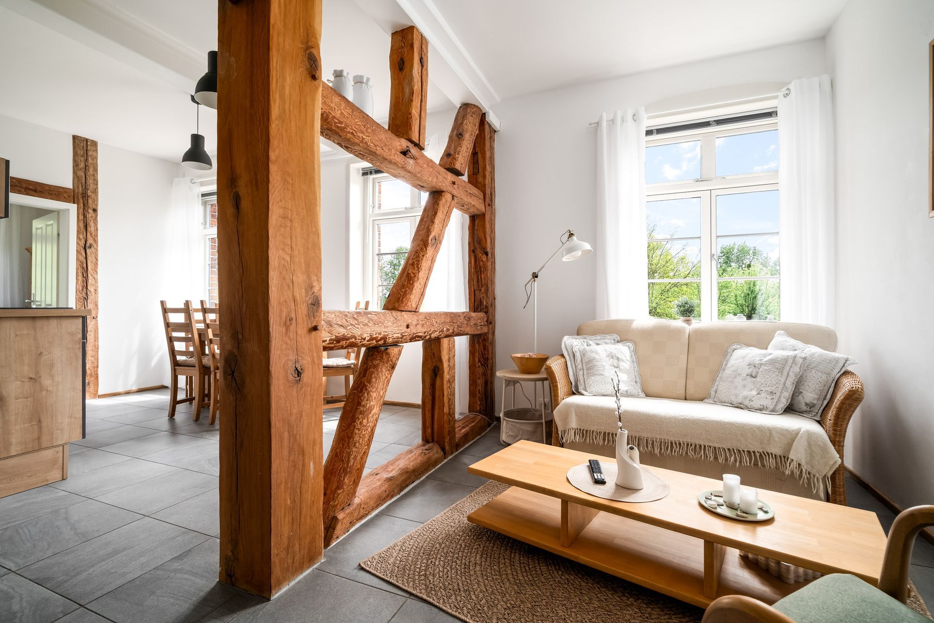 Helles Wohnzimmer mit sichtbaren Holzbalken, weißem Sofa und Couchtisch an einem sonnendurchfluteten Fenster