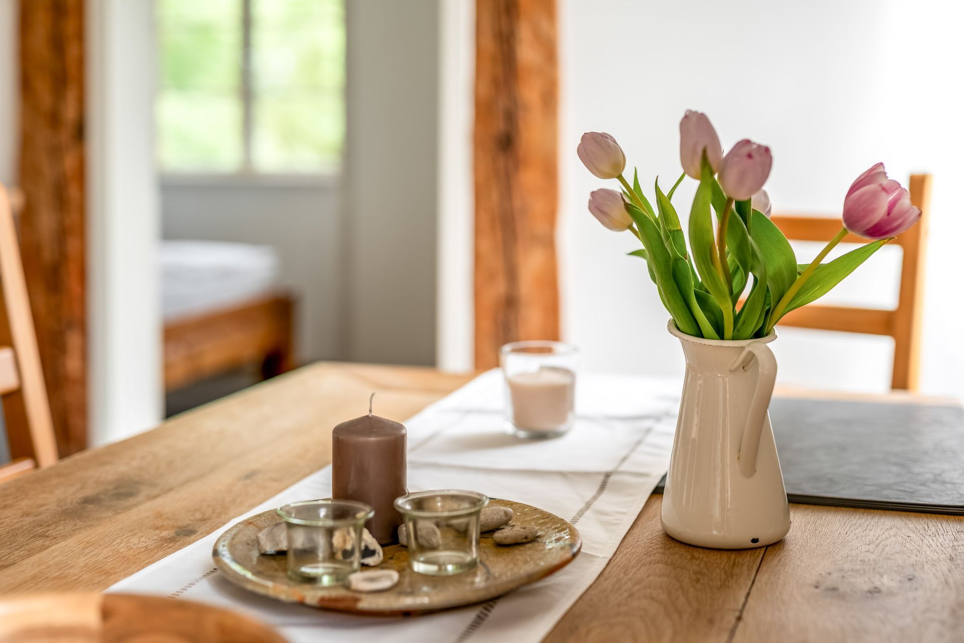 Ein hölzerner Frühstückstisch mit Tablett, Kaffeetasse und Vase mit rosa Tulpen in einem hellen Raum
