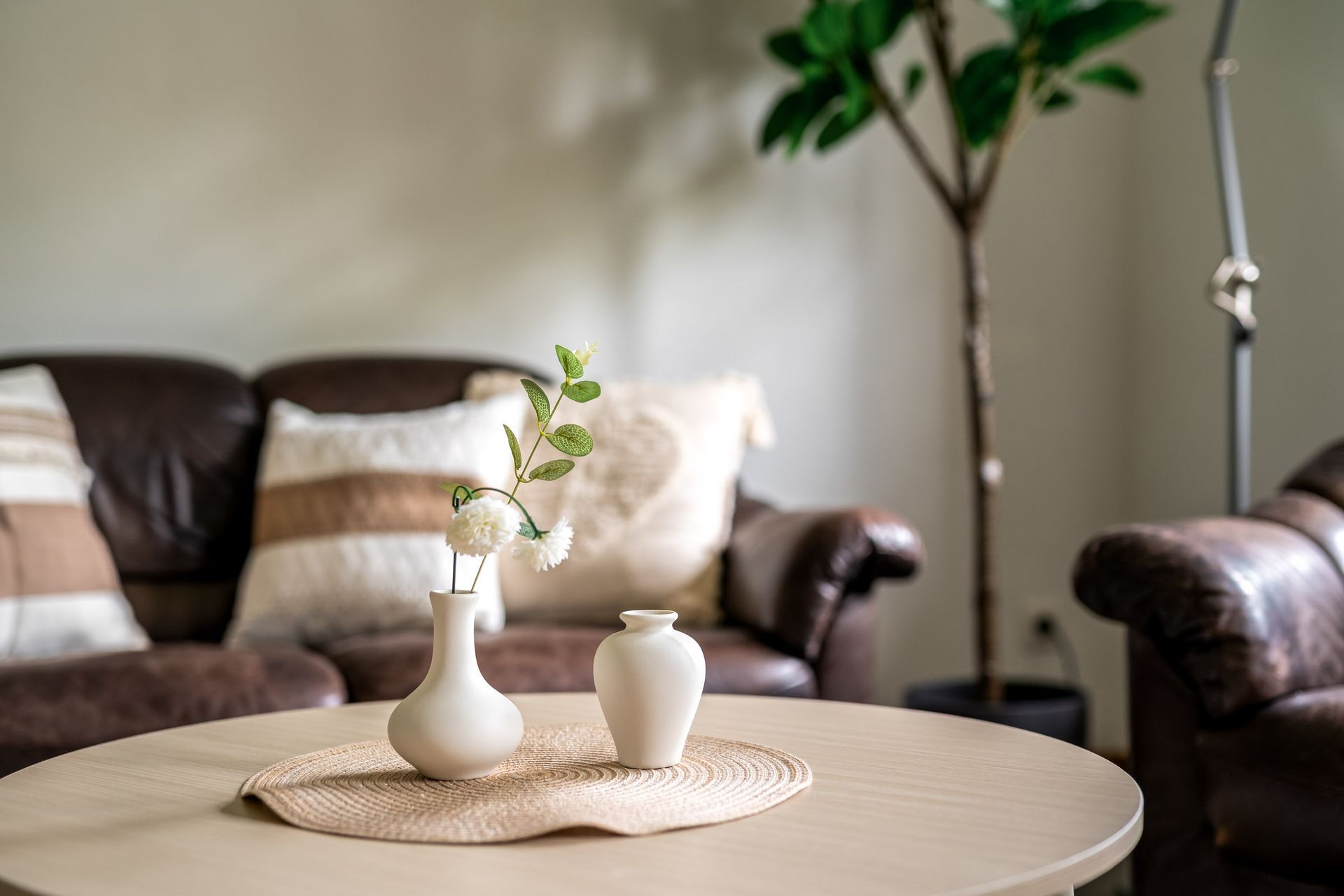 Gemütliches Wohnzimmer mit rundem Tisch, weißen Vasen und braunem Ledersofa im Hintergrund