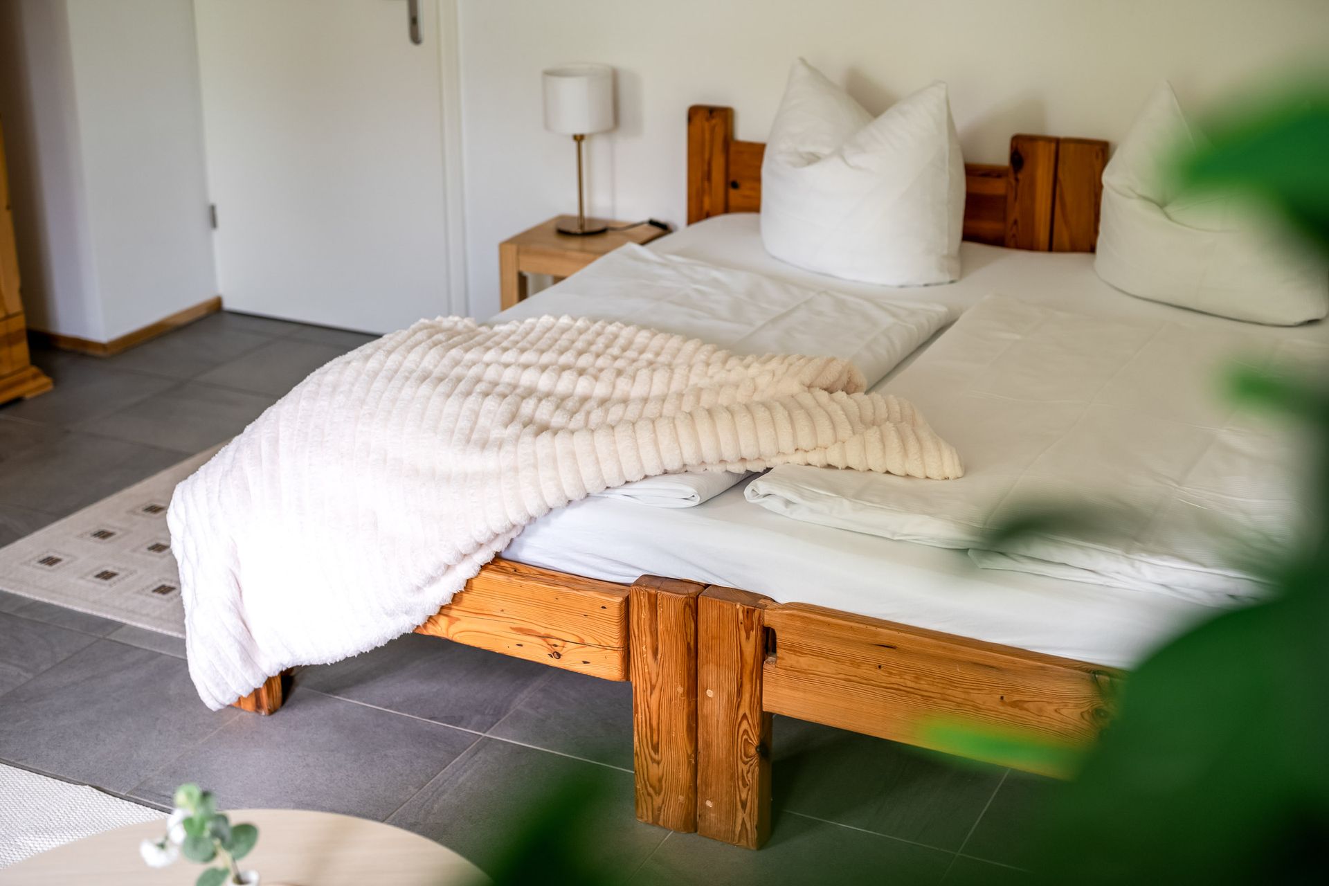 Weißes Bett mit zerknitterter Bettwäsche in einem hellen, minimalistischen Schlafzimmer mit Holzelementen und einer Nachttischlampe