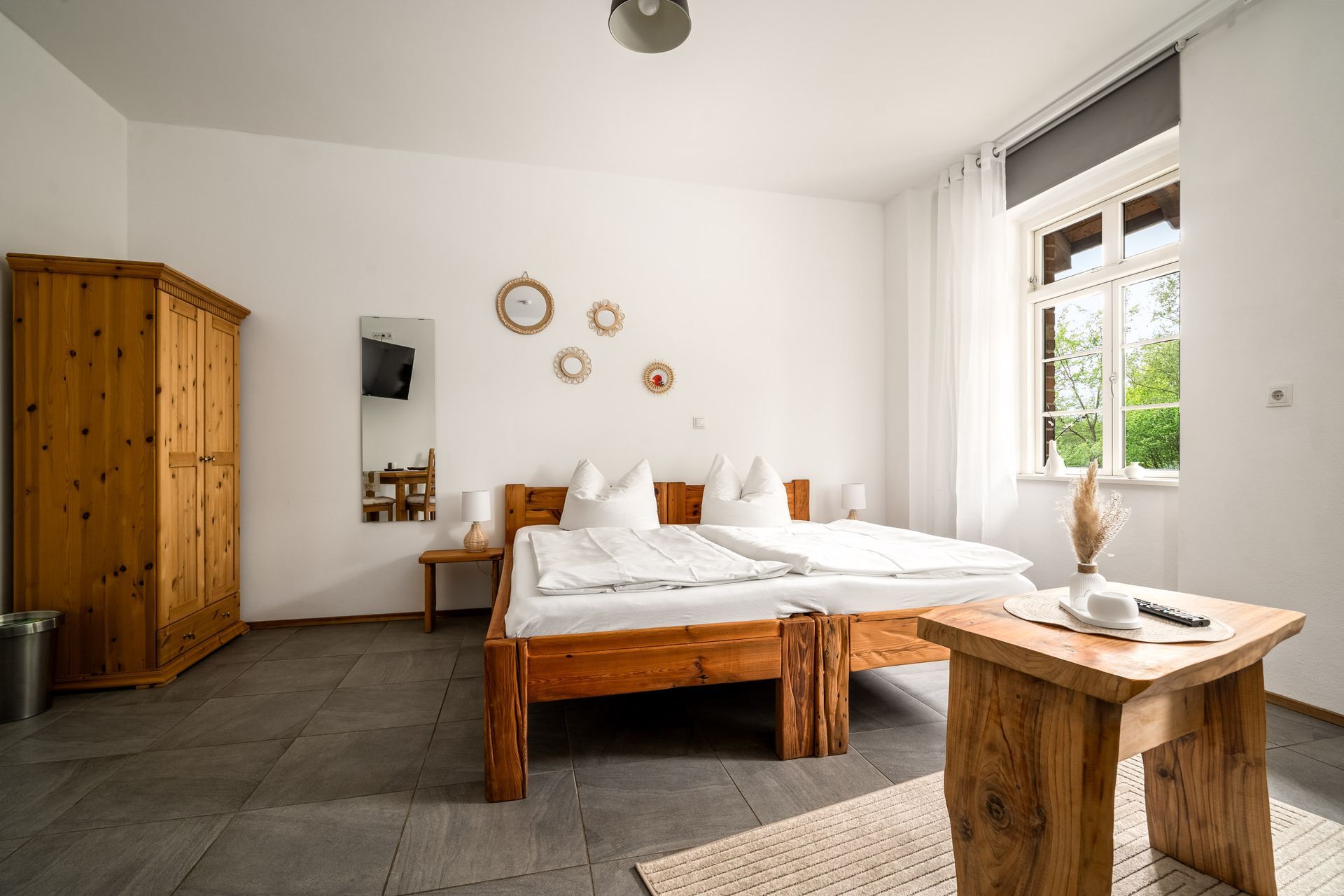 Helles, minimalistisches Schlafzimmer mit Holzbett, Bank, Kleiderschrank und großem Fenster, das Tageslicht hereinlässt