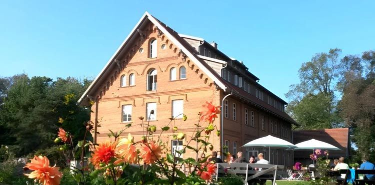 Backsteingebäude mit weißen Sonnenschirmen und Blumen in einer sonnigen Gartenlandschaft