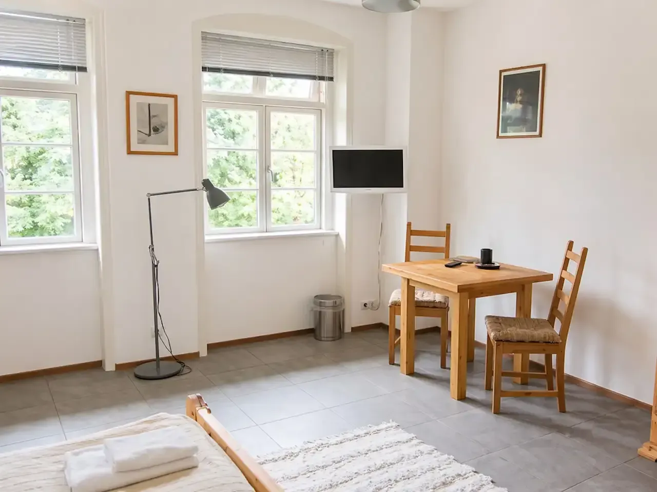 Minimalistisches Wohnzimmer mit Holztisch, Stühlen, Fenstern, Lampe und kleinem Fernseher auf einem Ständer