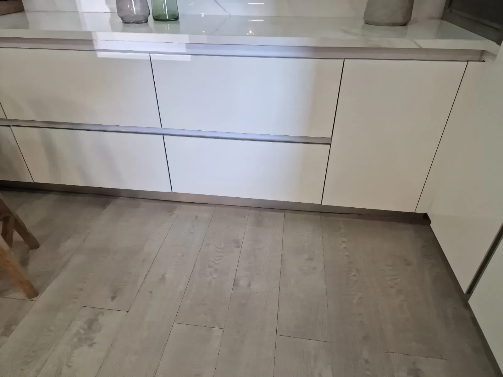 Armarios de cocina blancos con cajones y puertas sobre un suelo de madera clara.