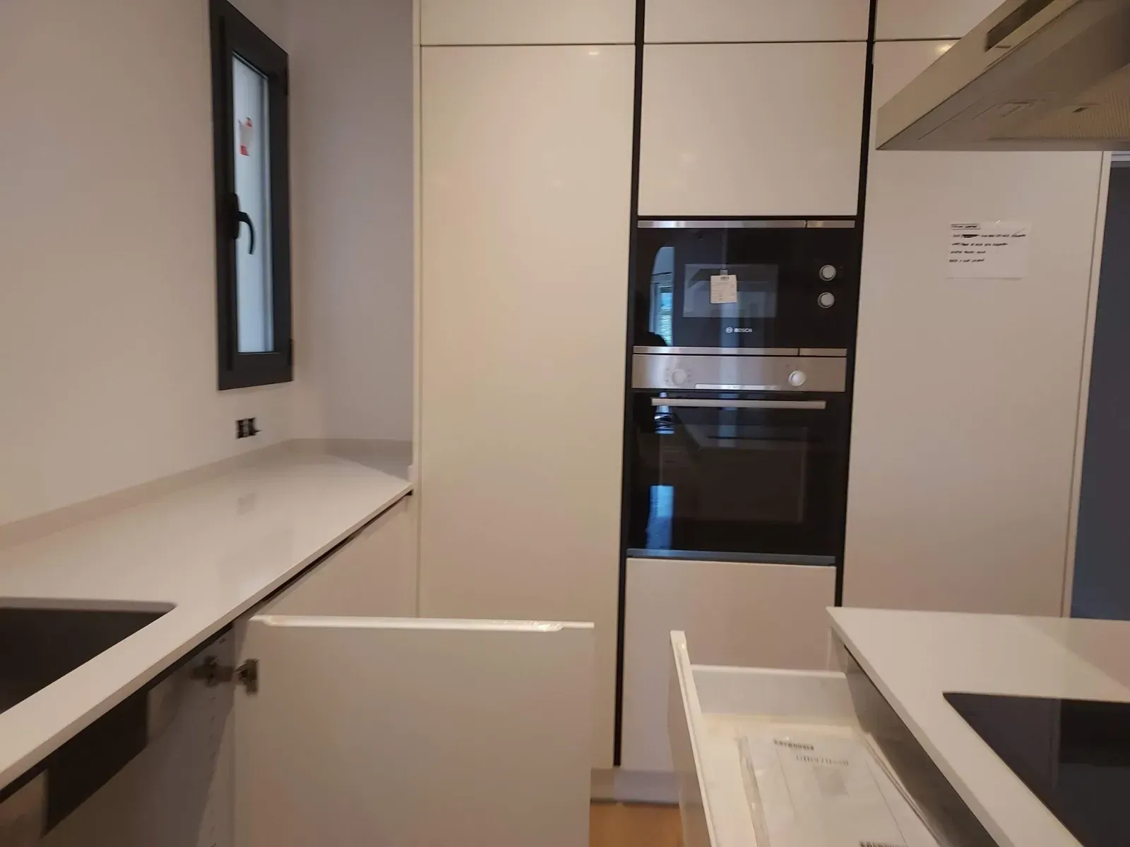 Cocina moderna blanca con horno empotrado, encimeras y una ventana sobre el fregadero.