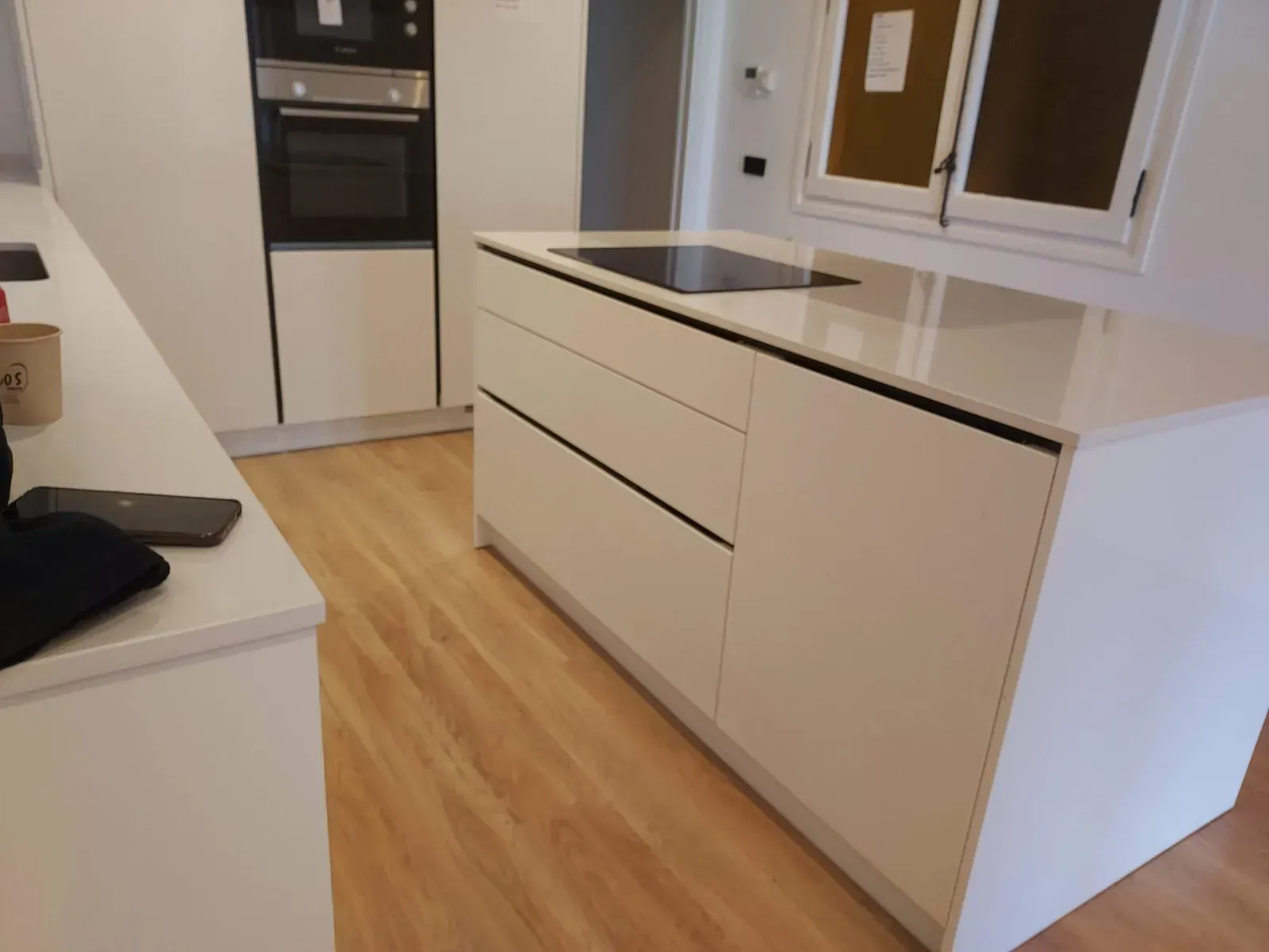Cocina moderna con isla blanca, encimera negra, horno empotrado y suelo de madera.