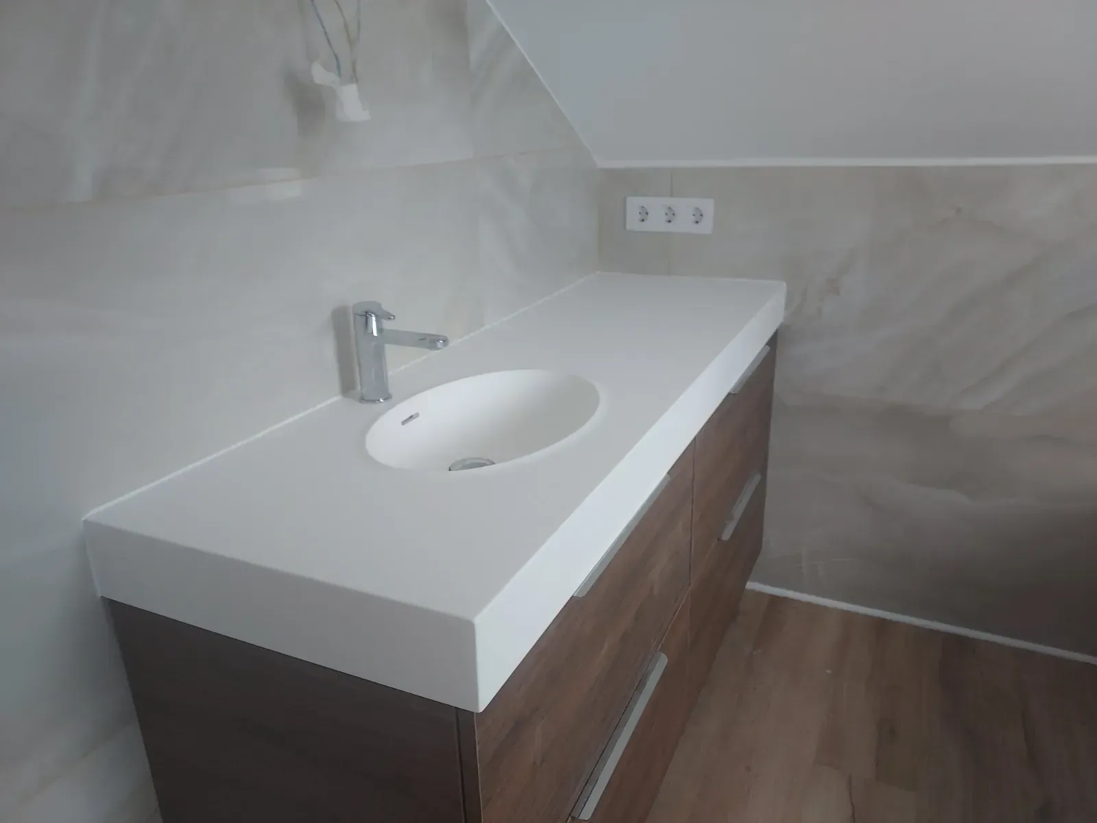 Tocador de baño moderno con encimera de lavabo blanca y grifo cromado bajo techo inclinado.