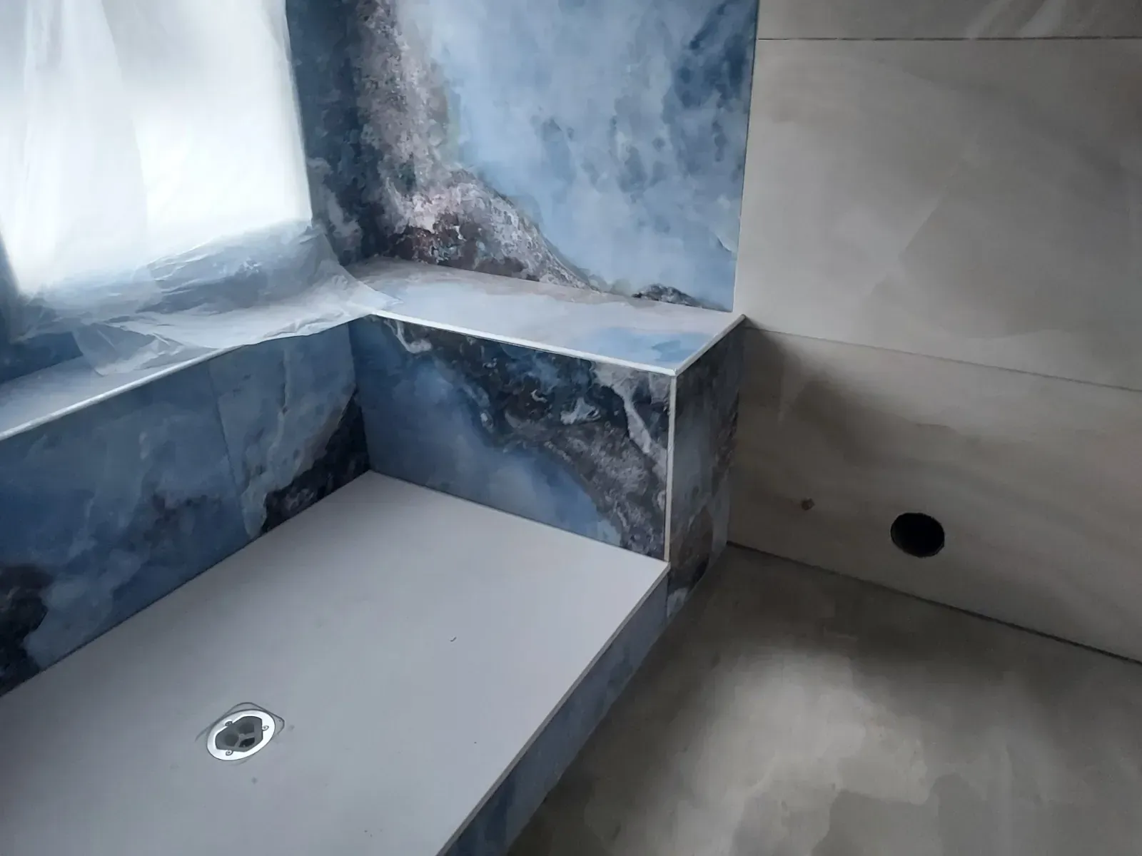 Rincón de ducha con azulejos azul grisáceos, banco incorporado y dos desagües.