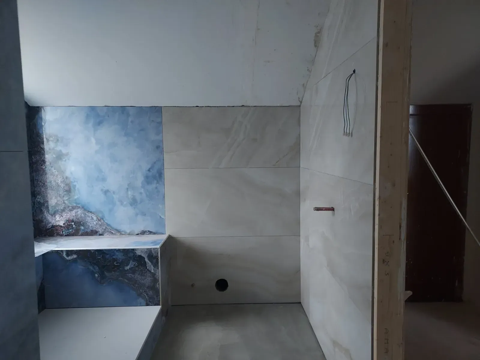 Baño parcialmente alicatado con pared de ducha, hueco para lavabo y azulejos decorativos texturizados azules.
