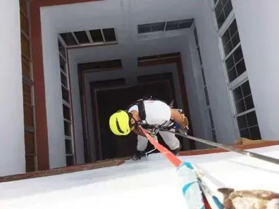 Una persona con un casco amarillo desciende en rápel por el hueco de un edificio alto utilizando cuerdas de seguridad.