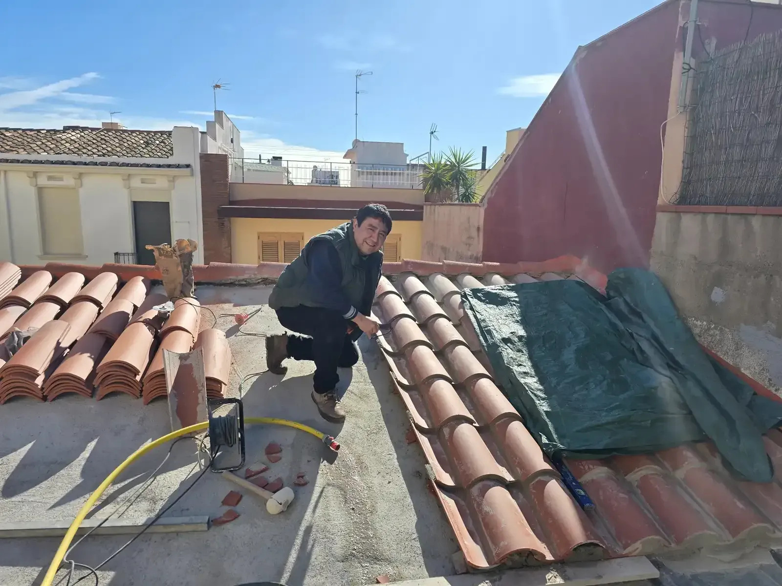 Un trabajador repara un tejado de tejas bajo la intensa luz del sol.
