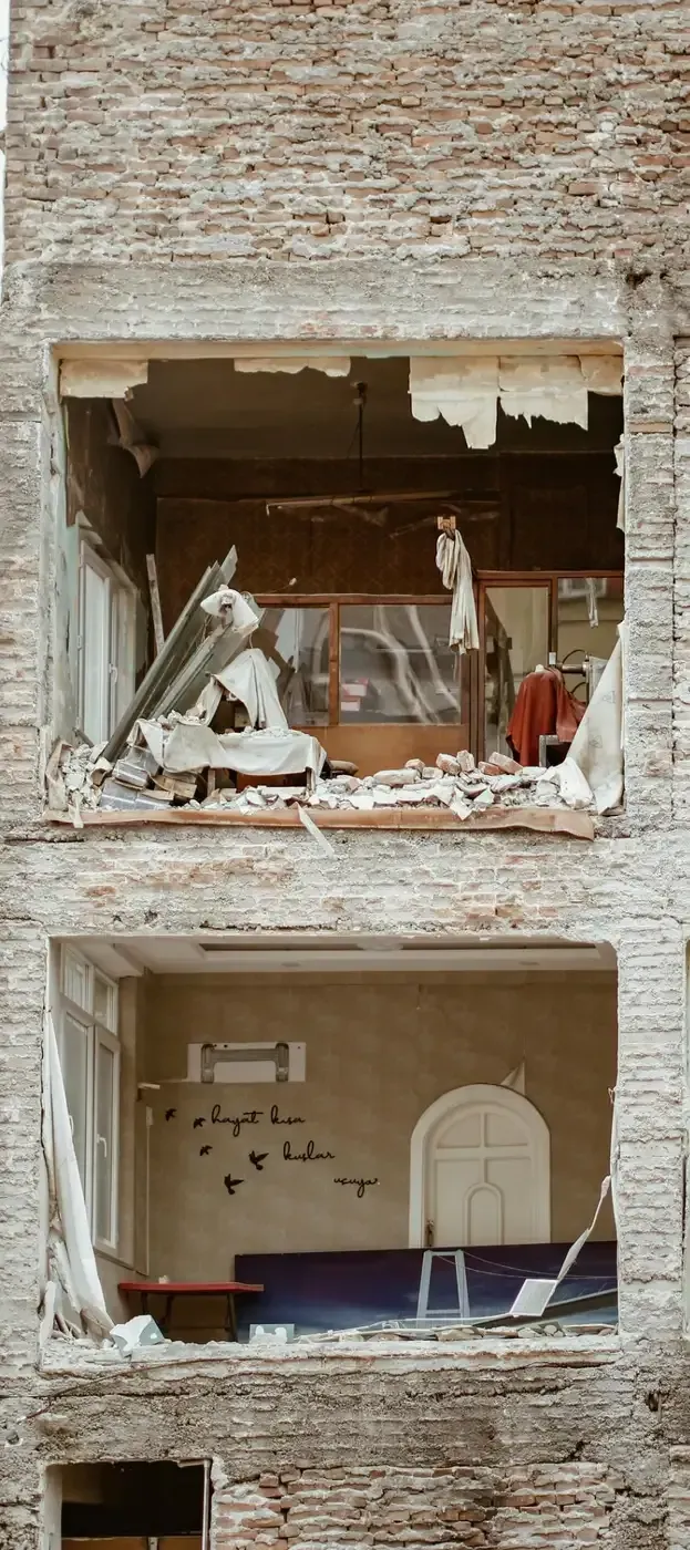 Edificio de ladrillo dañado con dos ventanas destrozadas y escombros en el interior.