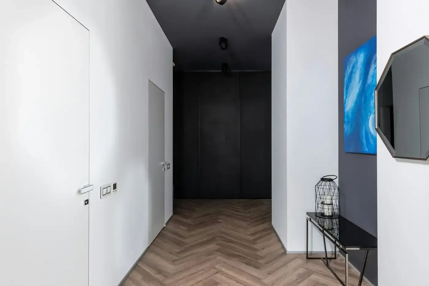 Pasillo moderno con paredes blancas, suelo con diseño de madera, techo oscuro y televisor montado en la pared a la derecha.