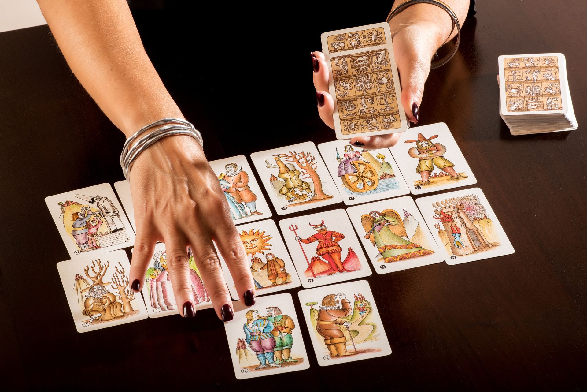 Personne avec les mains disposant des cartes de tarot sur une table, jeu tenu au-dessus.