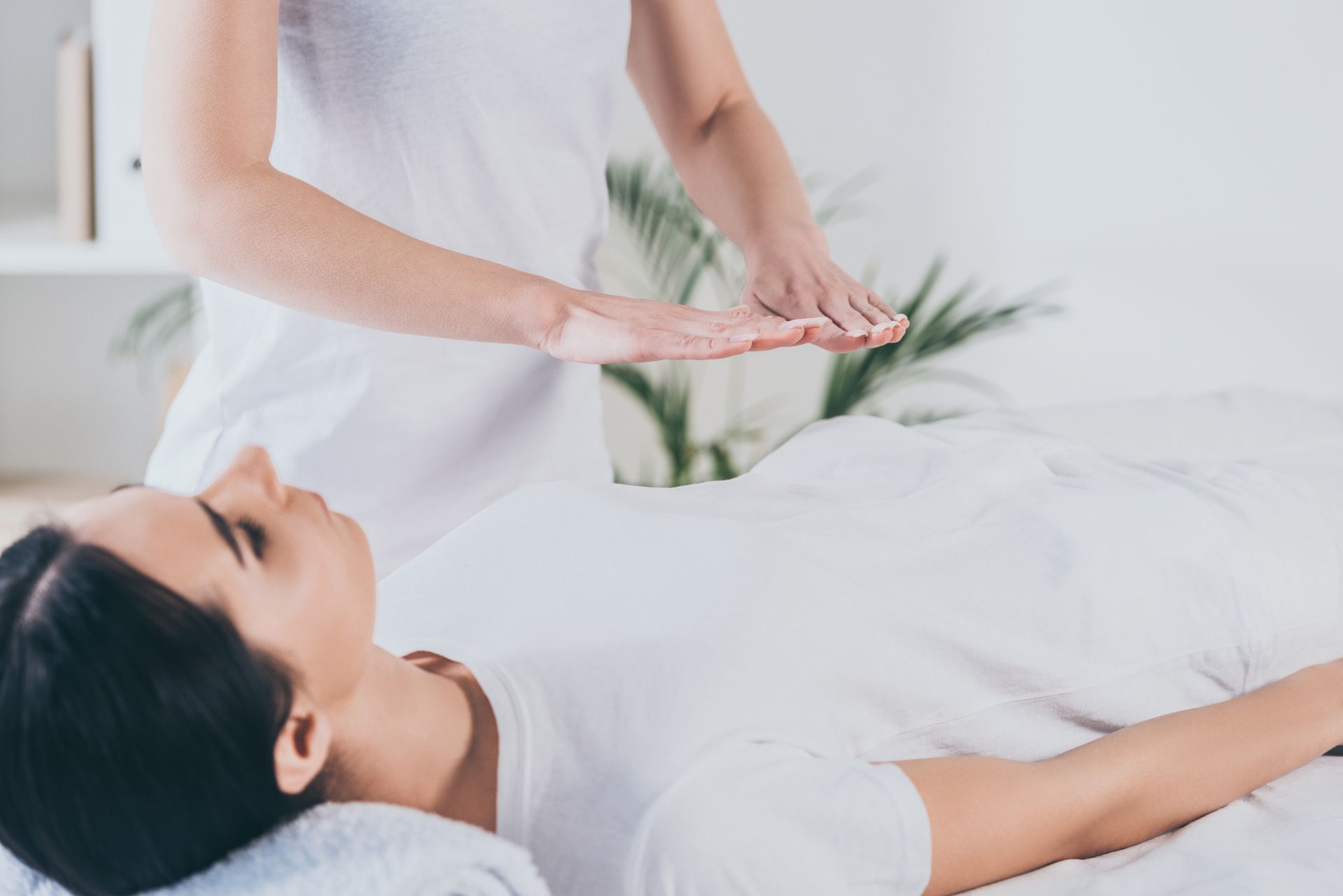Femme recevant du Reiki. Les mains du praticien sur son torse dans un décor clair.