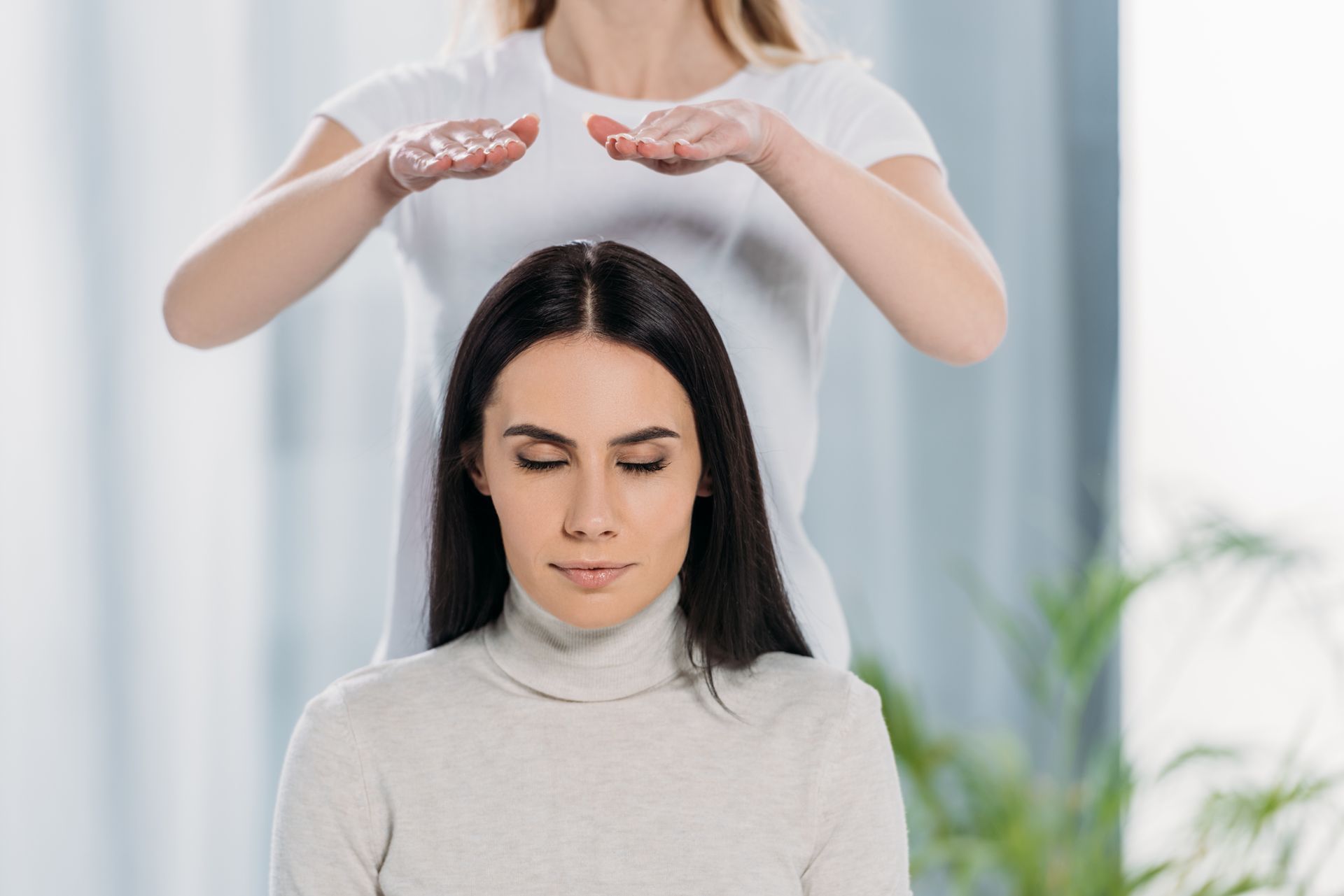 Femme recevant un soin énergétique, les mains au-dessus de la tête, les yeux fermés dans une pièce.