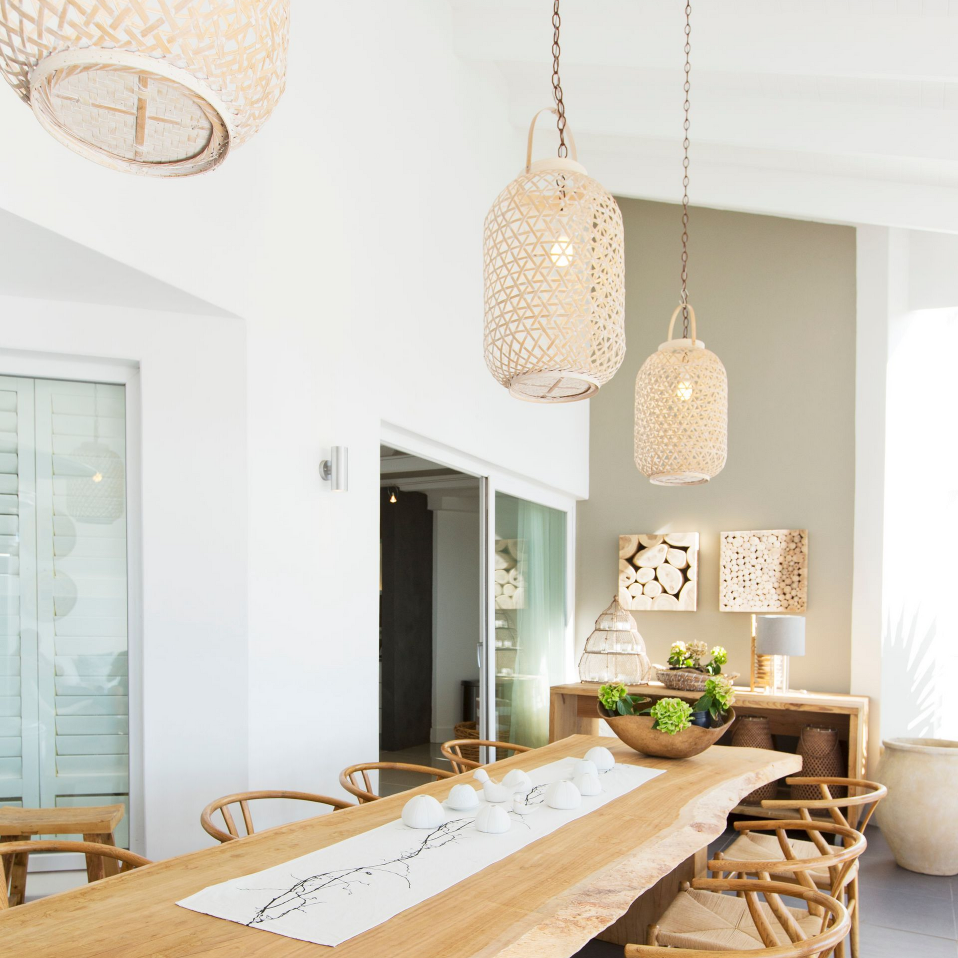 Salle à manger avec table en bois, luminaires tissés et chaises; palette de couleurs neutres.