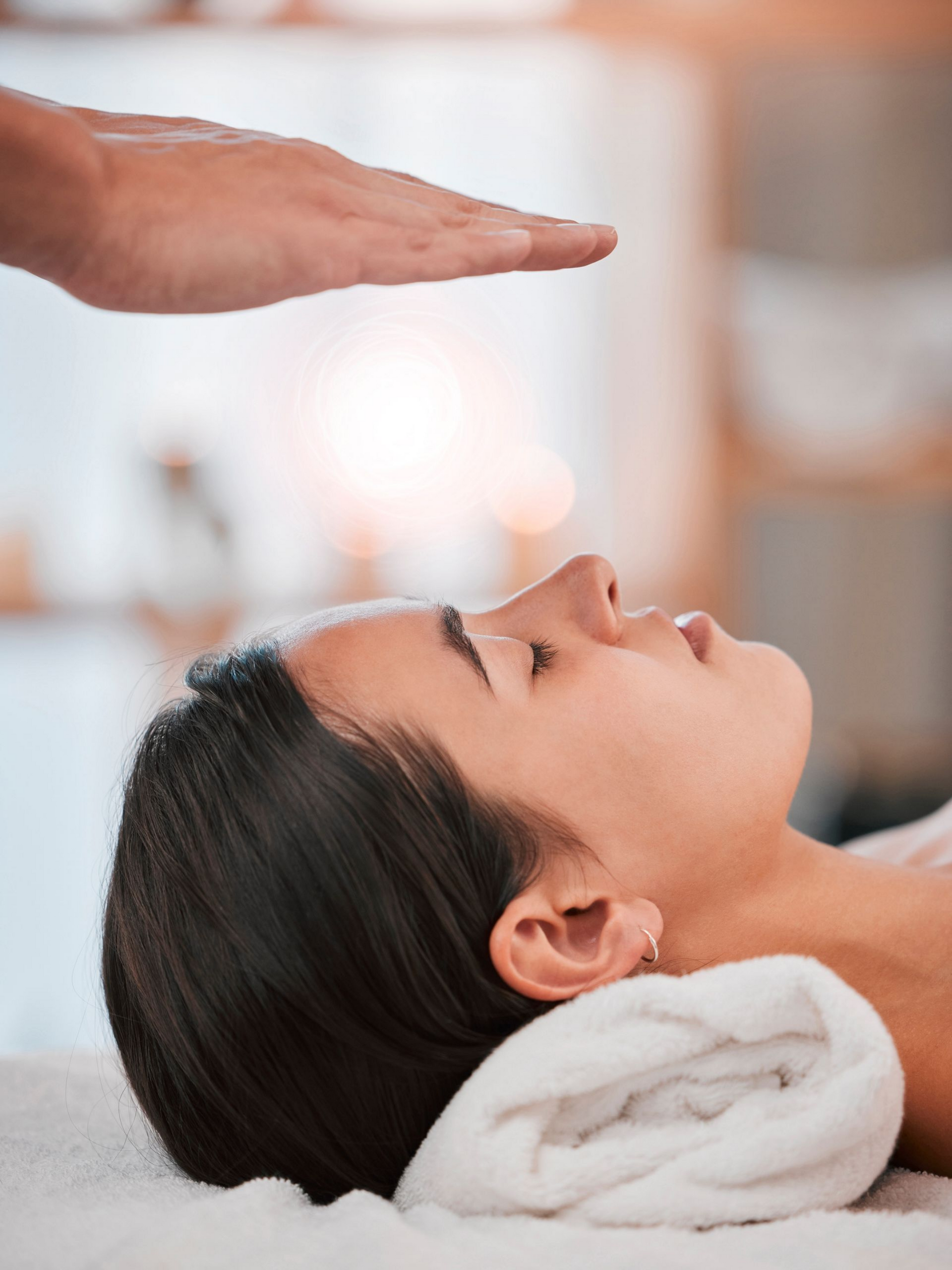 Femme recevant un soin énergétique, main au-dessus de la tête, yeux fermés, cadre spa.