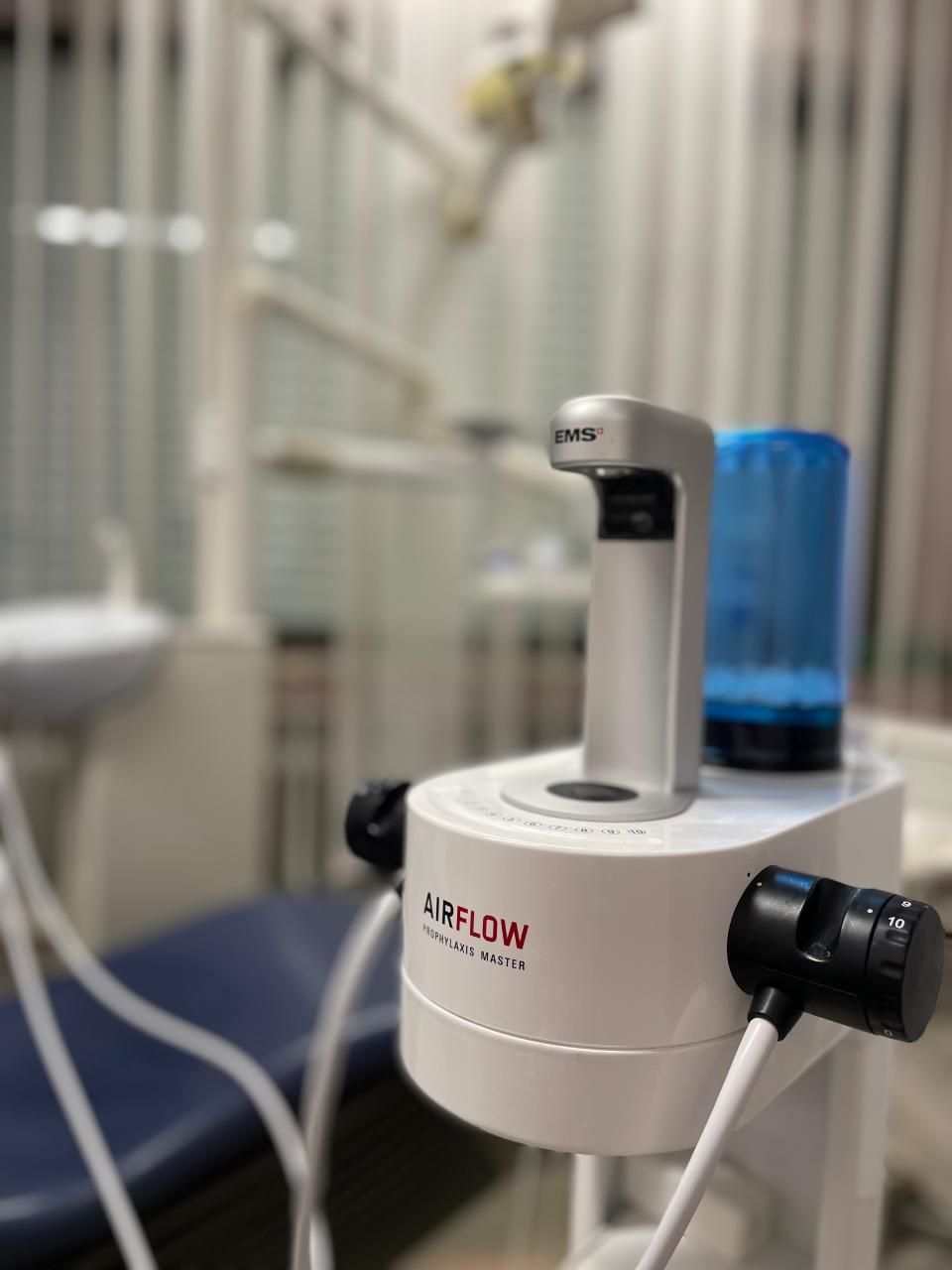 Zahnarztpraxis mit einer weißen Behandlungseinheit. Im Vordergrund steht ein silbernes Gerät mit „FLOW“.