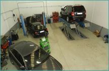 Taller de reparación de automóviles con varios coches en los elevadores y un carro de servicio verde en primer plano