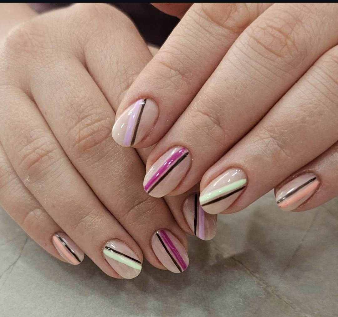 Manos con manicura a rayas en tonos pastel: rosa, menta y beige.
