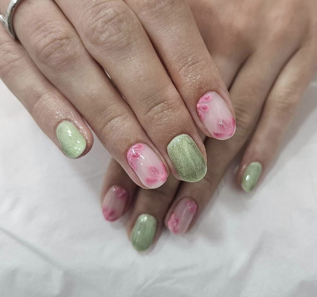Manos con uñas pintadas de rosa y verde, descansando juntas sobre una superficie blanca.