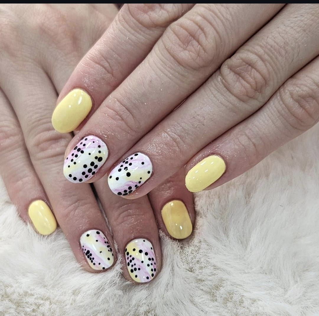 Primer plano de manos con manicura moteada en amarillo pastel y blanco sobre un fondo suave y peludo.