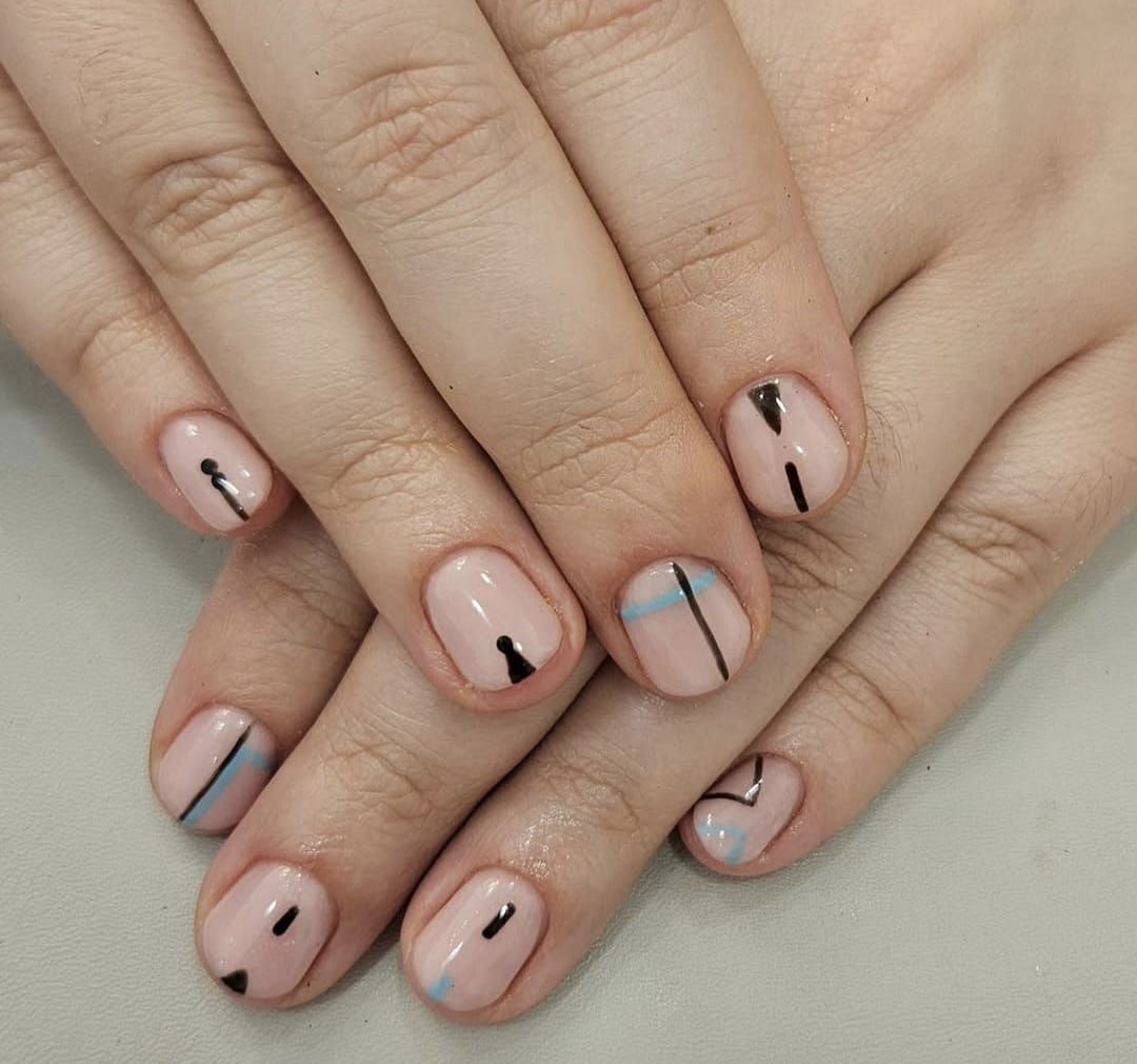 Manos con uñas de color rosa pálido y un diseño de uñas con finas líneas negras, azules y doradas.