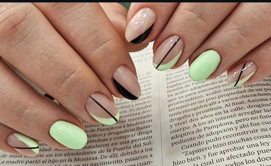 Manos con uñas decoradas en tonos verde pastel y nude, apoyadas sobre la página de un libro abierto.