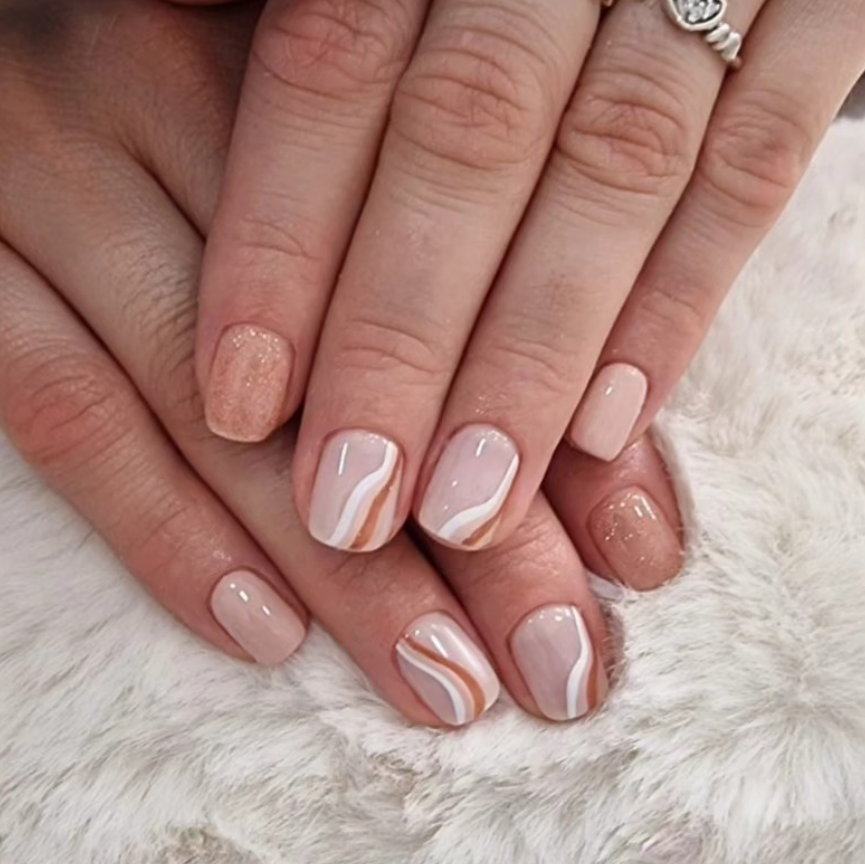 Primer plano de manos bien cuidadas con uñas decoradas en tonos nude y mármol blanco sobre un fondo blanco suave.