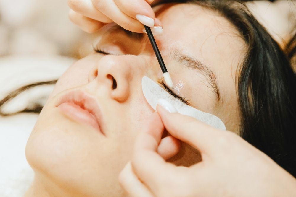 Una cosmetóloga aplica maquillaje de cejas con un pincel a una clienta que está tumbada.
