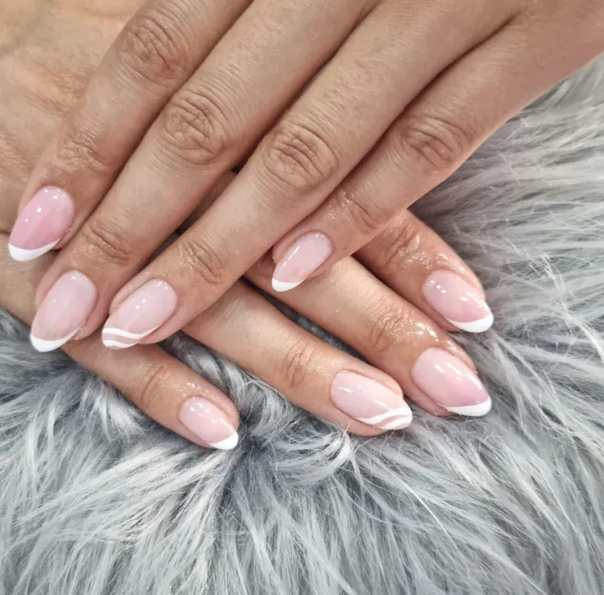 Manos con uñas pintadas de un rosa pálido brillante, descansando sobre una superficie de suave piel sintética gris.