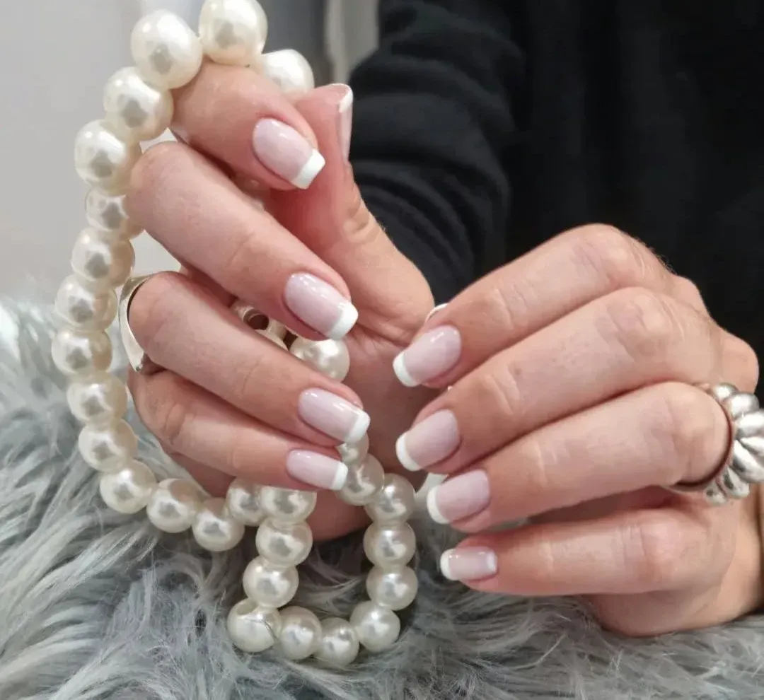 Manos que sostienen un collar y una pulsera de perlas sobre una superficie de piel gris