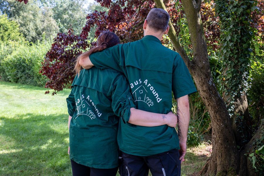 Zwei Personen in grünen Hemden stehen in einem sonnigen Garten und haben die Arme umeinander geschlungen.