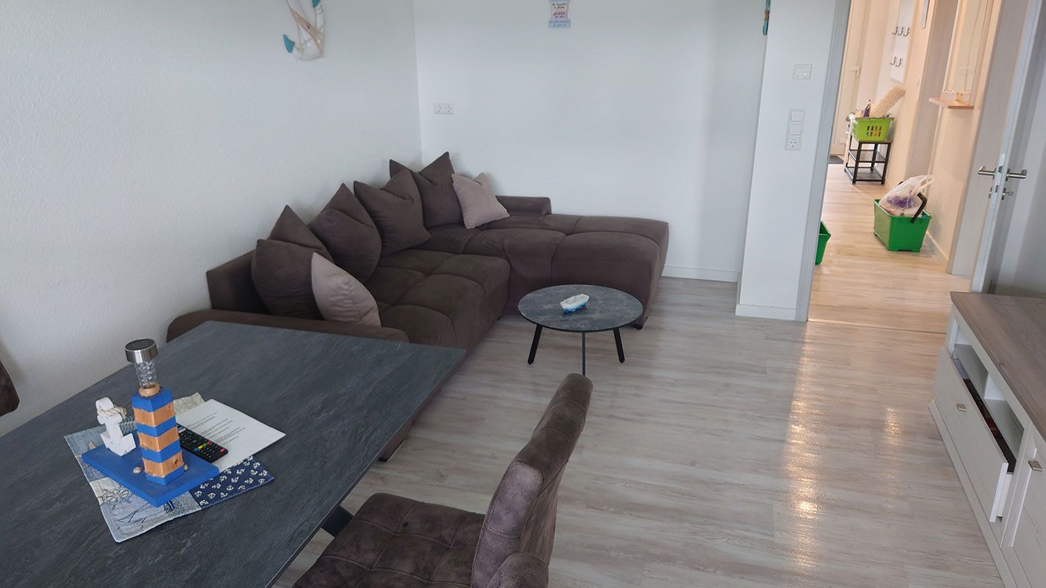 Modernes Wohnzimmer mit dunklem Ecksofa, niedrigen Beistelltischen und einem Flur, der zur Küche führt.